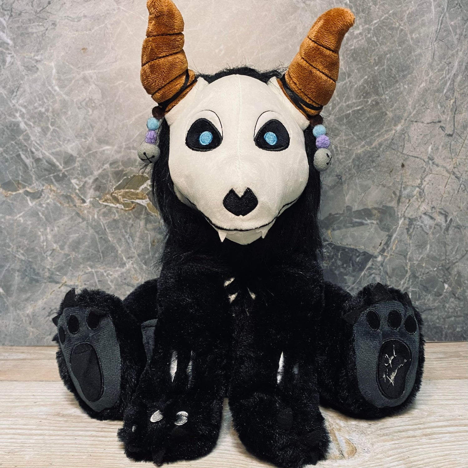 A plush toy featuring Orpheus from A Soul to Keep with bead charms, horns, and a fluffy tail, sitting upright.